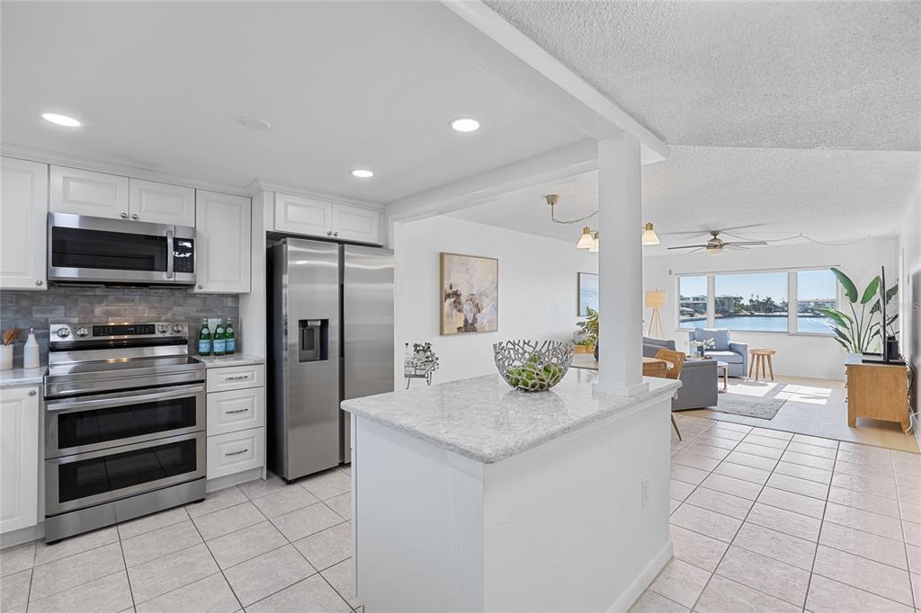 A kitchen with white cabinets, stainless steel appliances, and a granite island overlooks a living area — 4775 COVE CIRCLE UNIT 203, ST PETERSBURG, FL