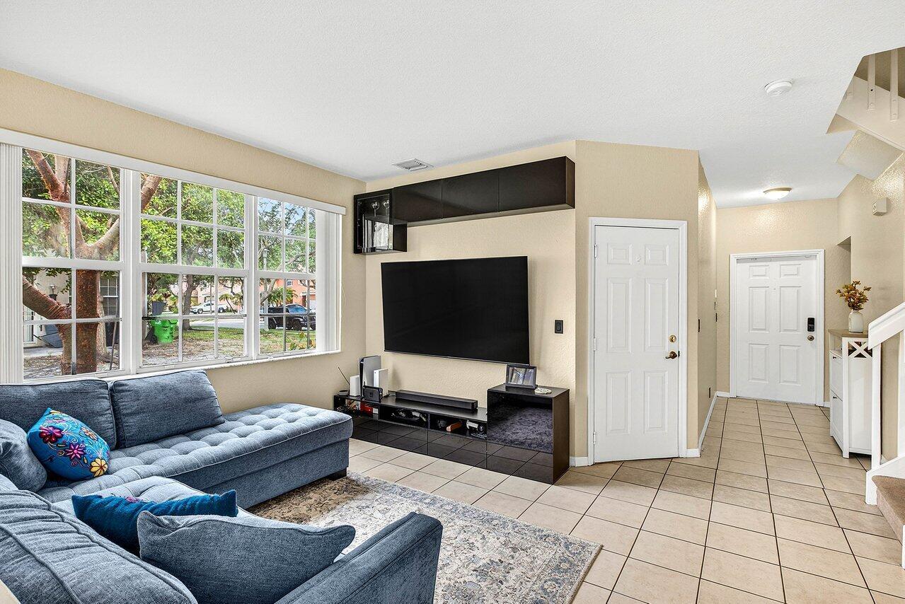 A living room features a blue sectional sofa, a wall-mounted television, and tile flooring — 9090 NW 40th Place, Sunrise FL 33351, SUNRISE, FL