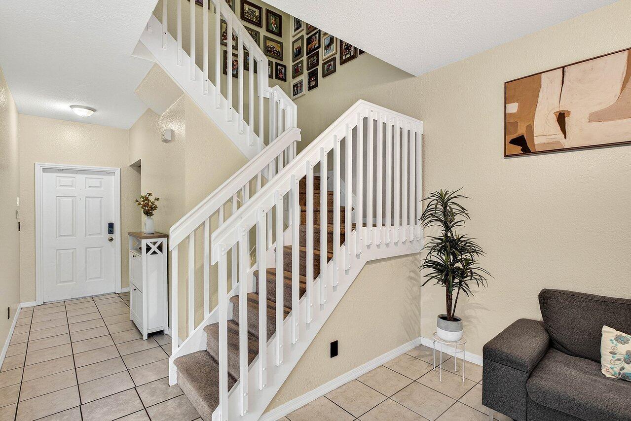 An entryway features a carpeted staircase with white railings, tile flooring, and a gray sofa — 9090 NW 40th Place, Sunrise FL 33351, SUNRISE, FL