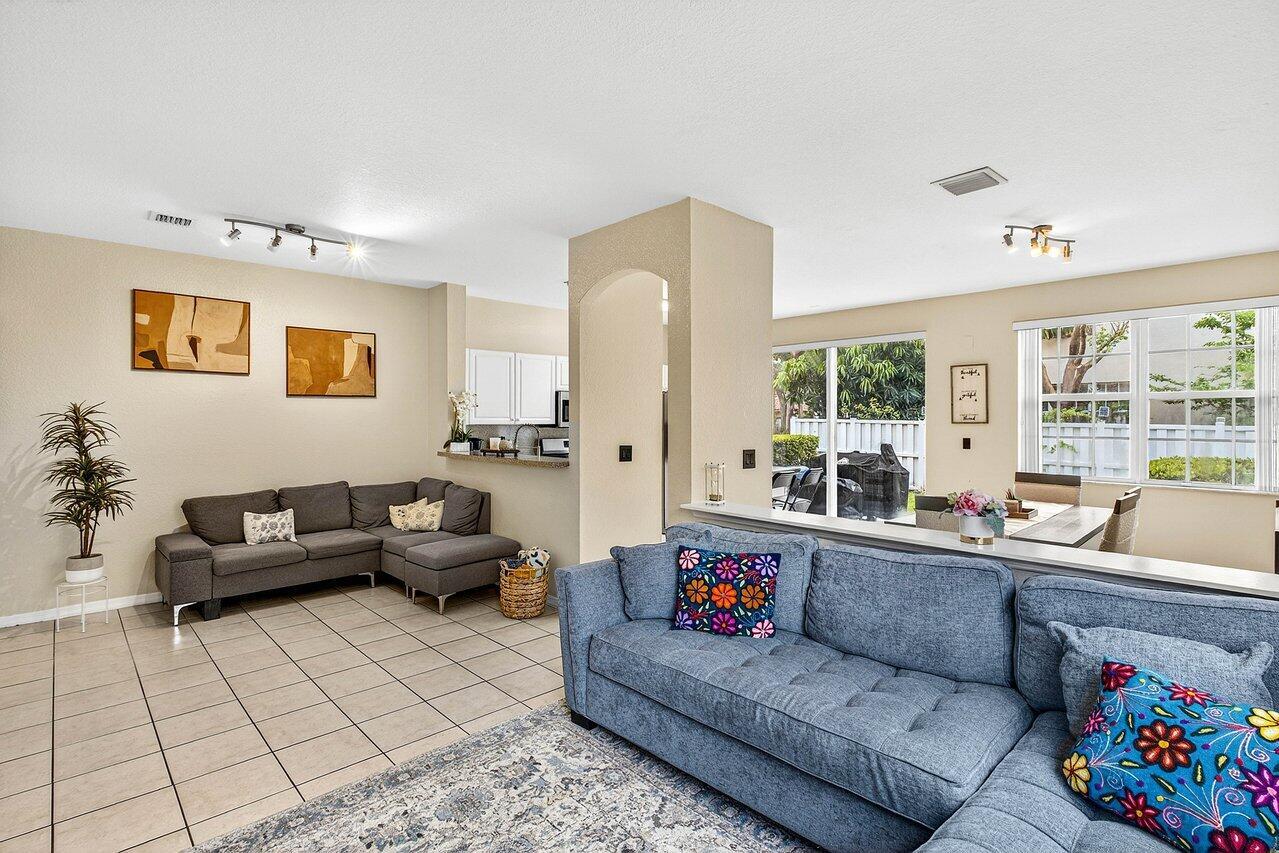 A living room with two grey sofas, tile flooring, and an open view into the kitchen — 9090 NW 40th Place, Sunrise FL 33351, SUNRISE, FL