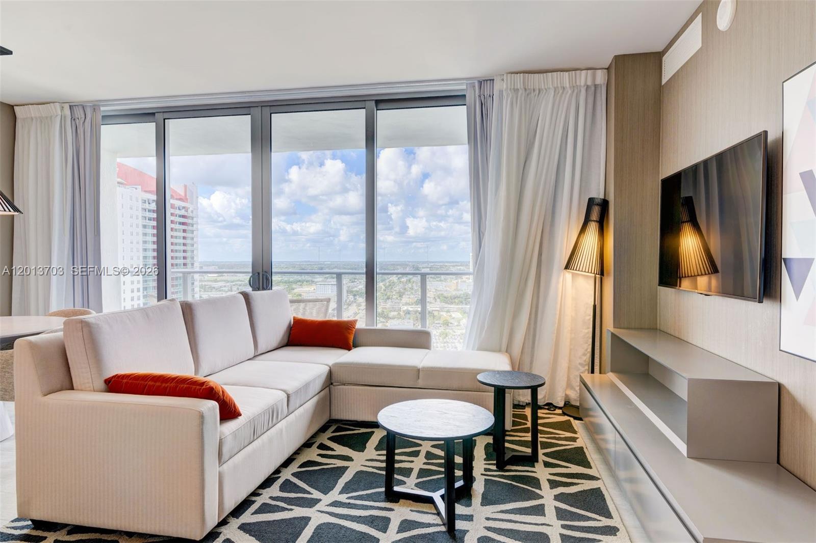 A living room features a sectional sofa, two round tables, a television, and floor-to-ceiling windows — 4010 S Ocean Dr # R2106, Hollywood FL 33019, HOLLYWOOD, FL