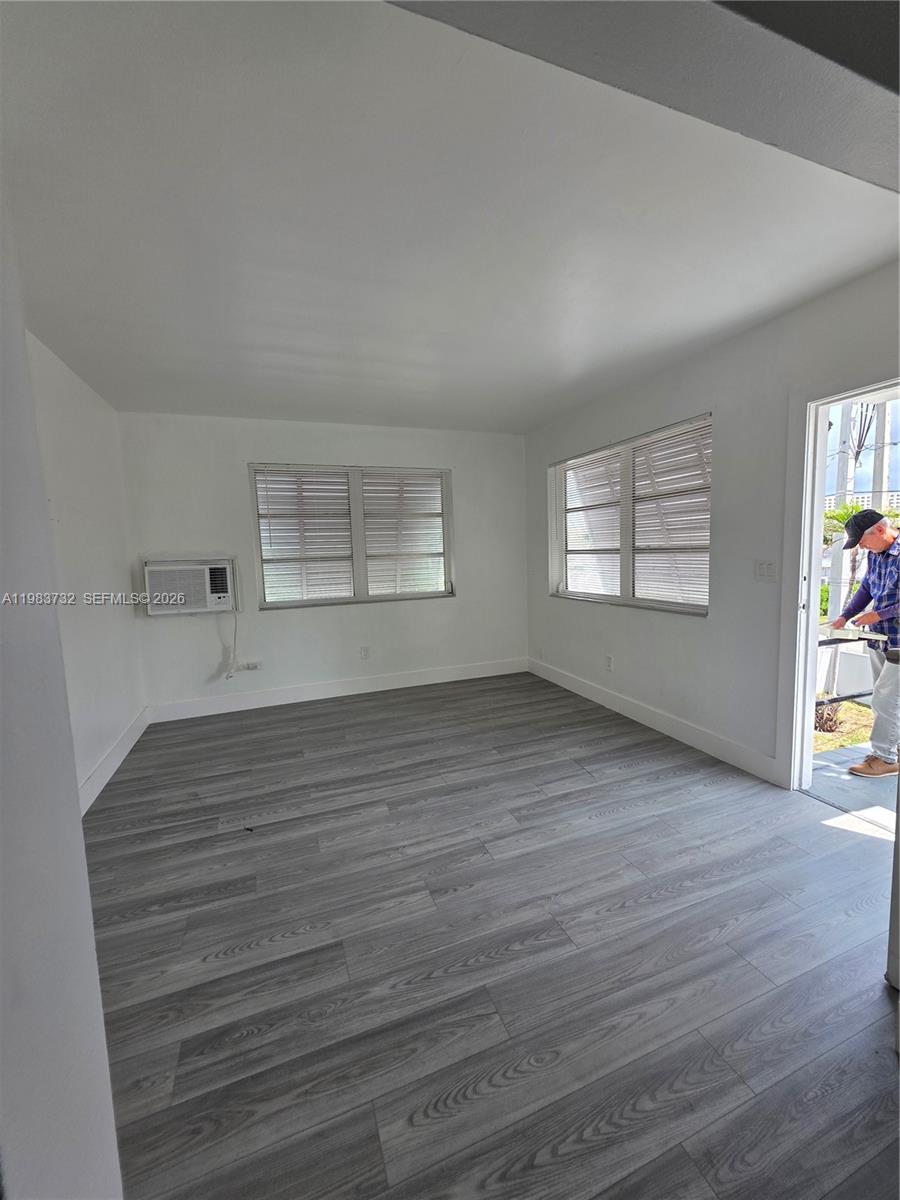 An empty room features white walls, gray wood-look flooring, two windows, and a wall-mounted air conditioner — 71 Esplanade Dr # D, Miami Springs FL 33166, MIAMI SPRINGS, FL