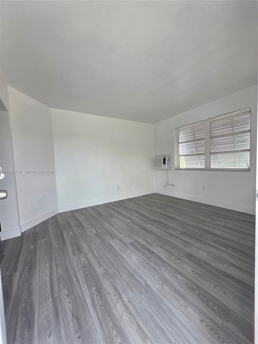 An empty room features white walls, gray wood-look flooring, and a window with blinds — 71 Esplanade Dr # D, Miami Springs FL 33166, MIAMI SPRINGS, FL