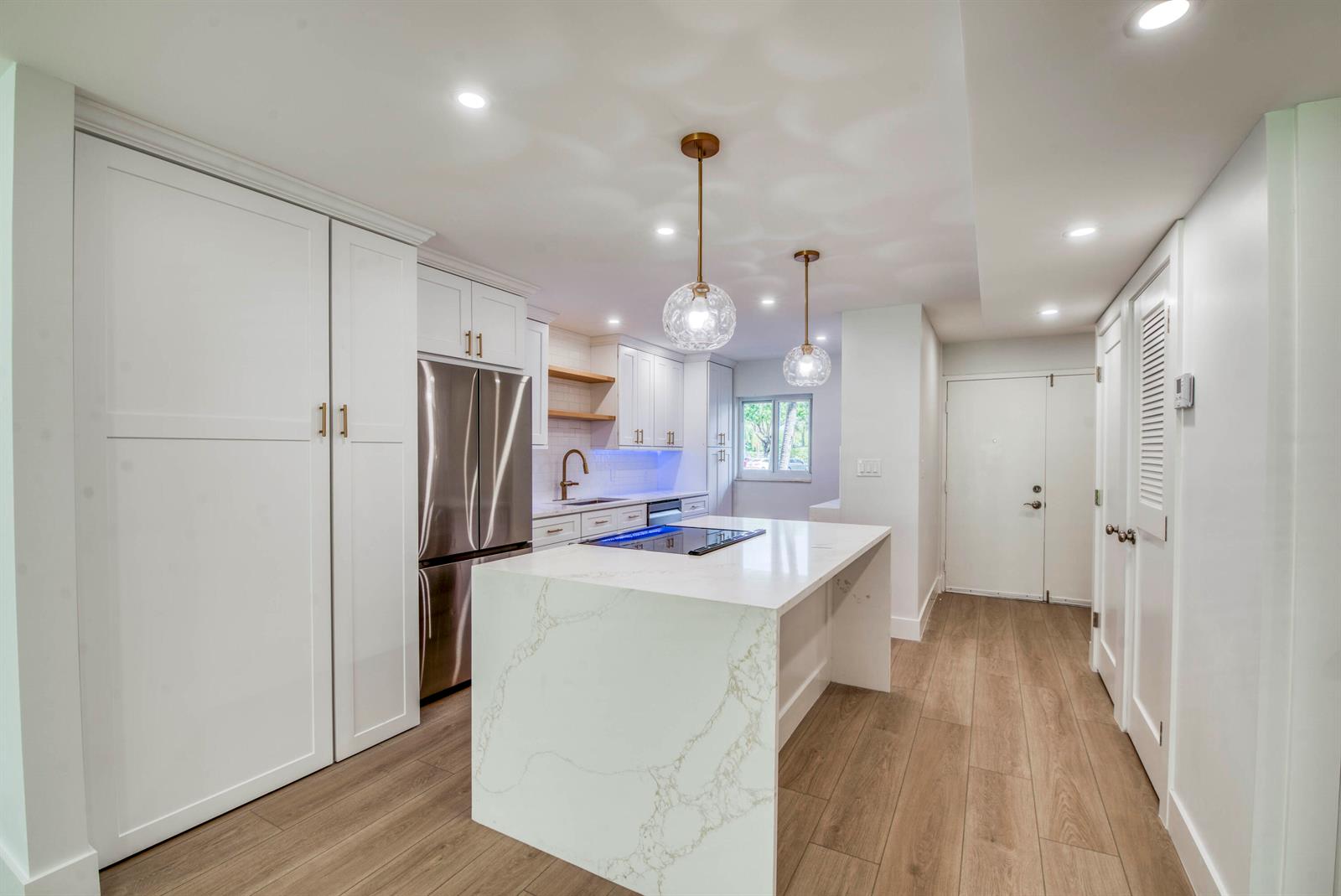 A modern kitchen features white cabinets, a marble-topped island, and an open living area beyond — 3326 Arcara Way # 104, Lake Worth FL 33467, LAKE WORTH, FL