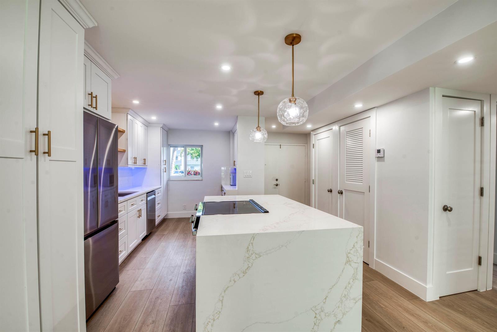 A modern kitchen features white cabinetry, a marble-topped island, stainless steel appliances, and wood flooring — 3326 Arcara Way # 104, Lake Worth FL 33467, LAKE WORTH, FL