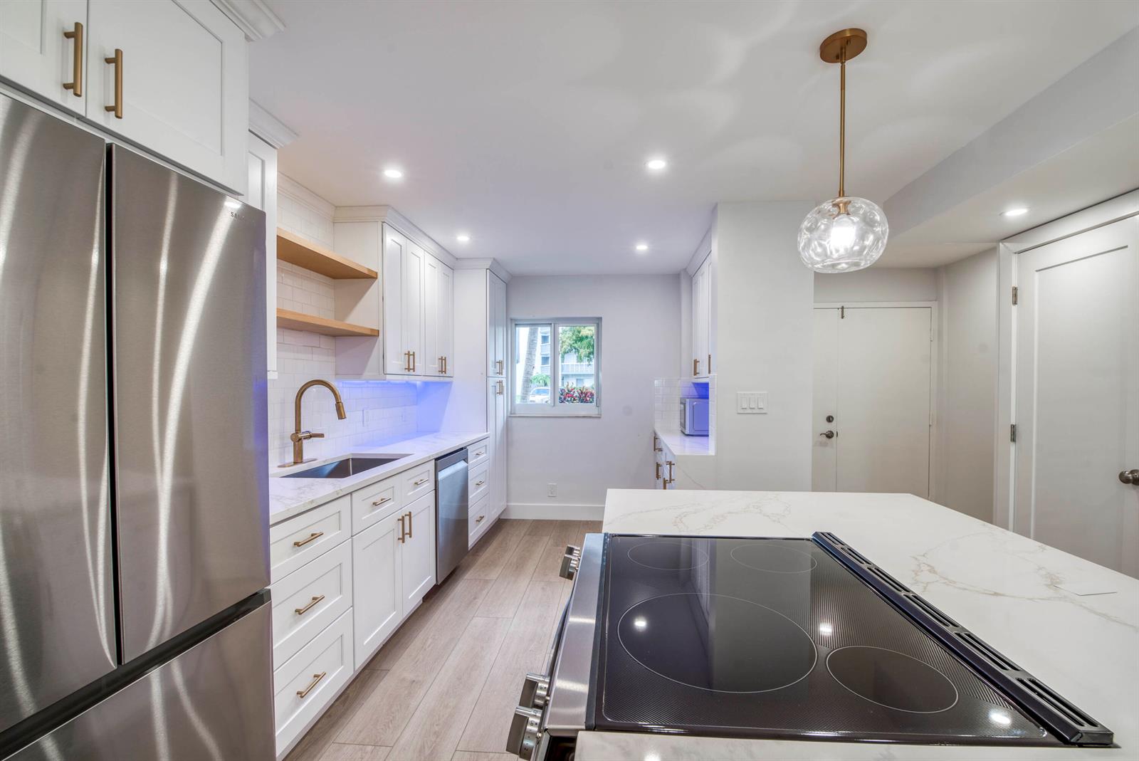 A modern kitchen features white cabinetry, a marble-topped island with a cooktop, and wood flooring — 3326 Arcara Way # 104, Lake Worth FL 33467, LAKE WORTH, FL