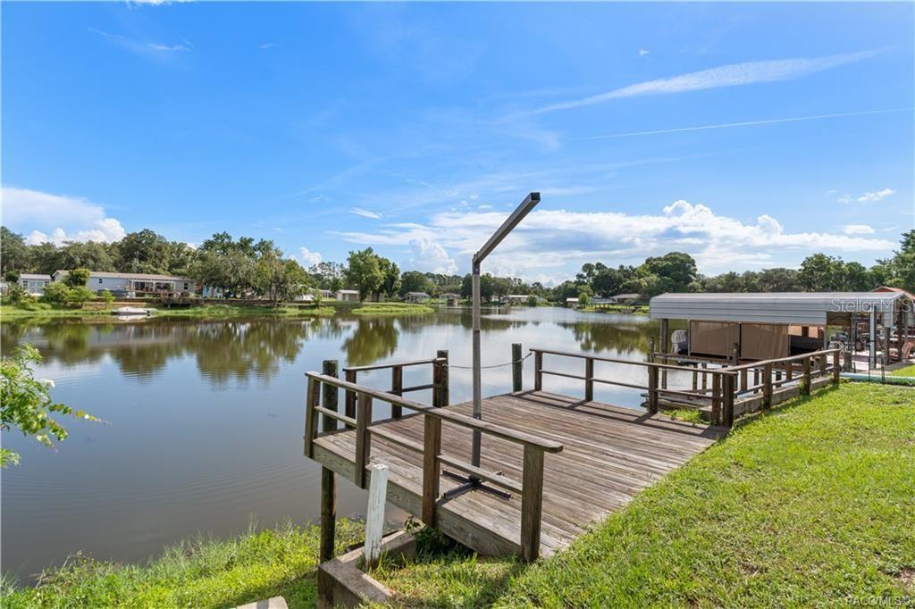 A wooden dock with a boat lift extends into a calm lake under a blue sky — 10312 E PIKE DRIVE, INVERNESS, FL