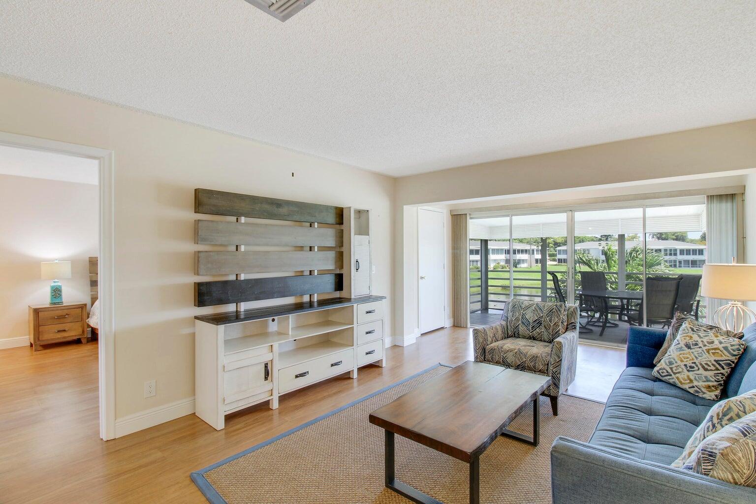 A living room with a wood media console, blue sofa, and sliding doors to a patio — 2730 SW 13th Street # 203, Delray Beach FL 33445, DELRAY BEACH, FL