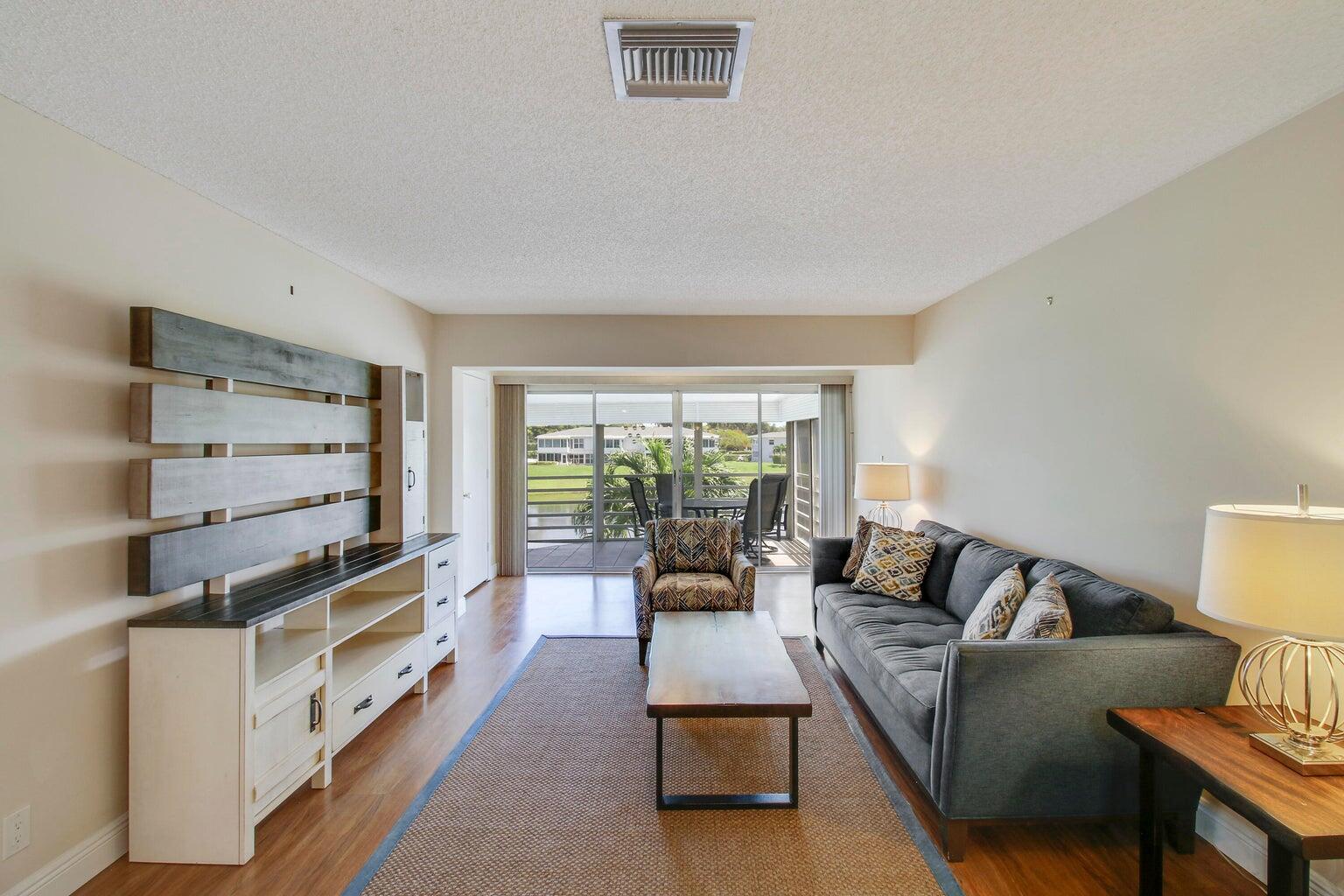 A living room features a grey sofa, wood media console, and sliding doors to a balcony — 2730 SW 13th Street # 203, Delray Beach FL 33445, DELRAY BEACH, FL