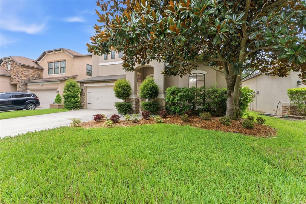 A two-story suburban house with a beige stucco exterior, a garage, and a large tree — 2515 CROSS MORE STREET, VALRICO, FL