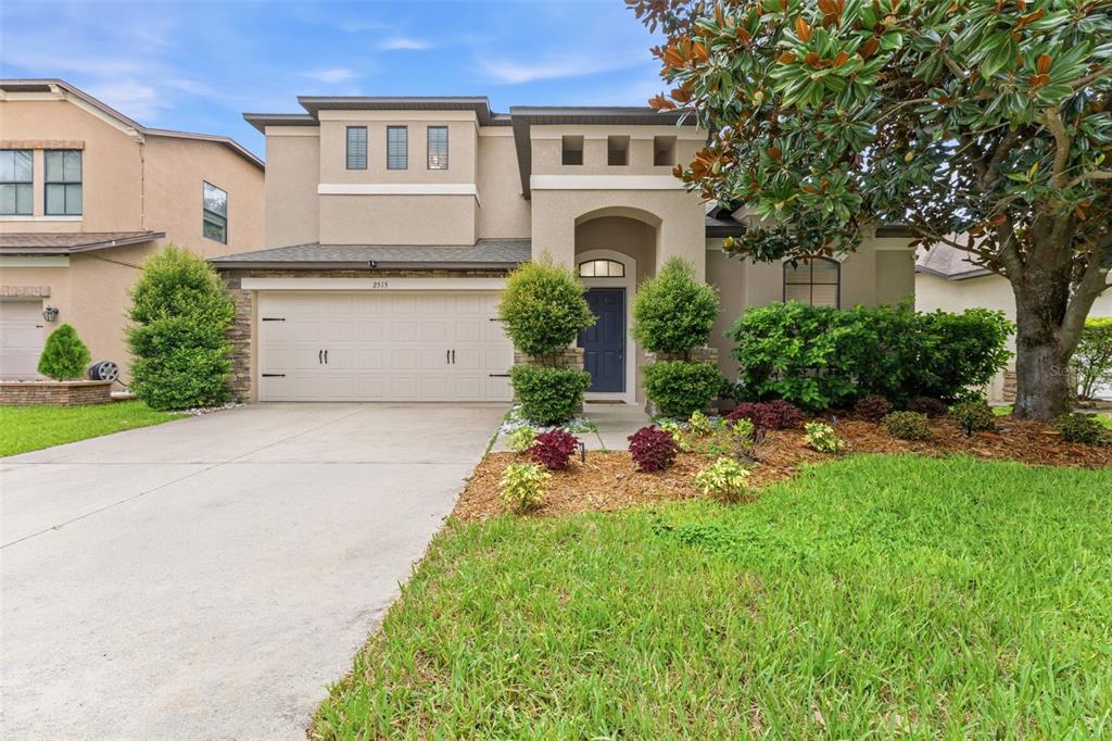 A two-story suburban house with a beige stucco exterior, a two-car garage, and landscaping — 2515 CROSS MORE STREET, VALRICO, FL