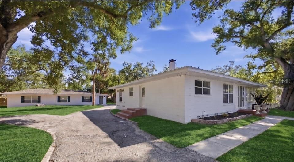A white single-story house with a paved driveway and large trees on a grassy lot — 3308 3RD AVENUE W, BRADENTON, FL