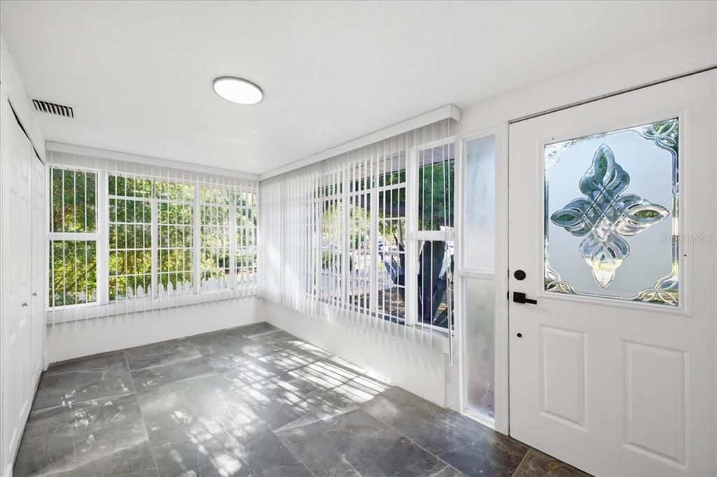 A sunroom features gray tile flooring, white walls, vertical blinds, and a decorative glass door — 3308 3RD AVENUE W, BRADENTON, FL