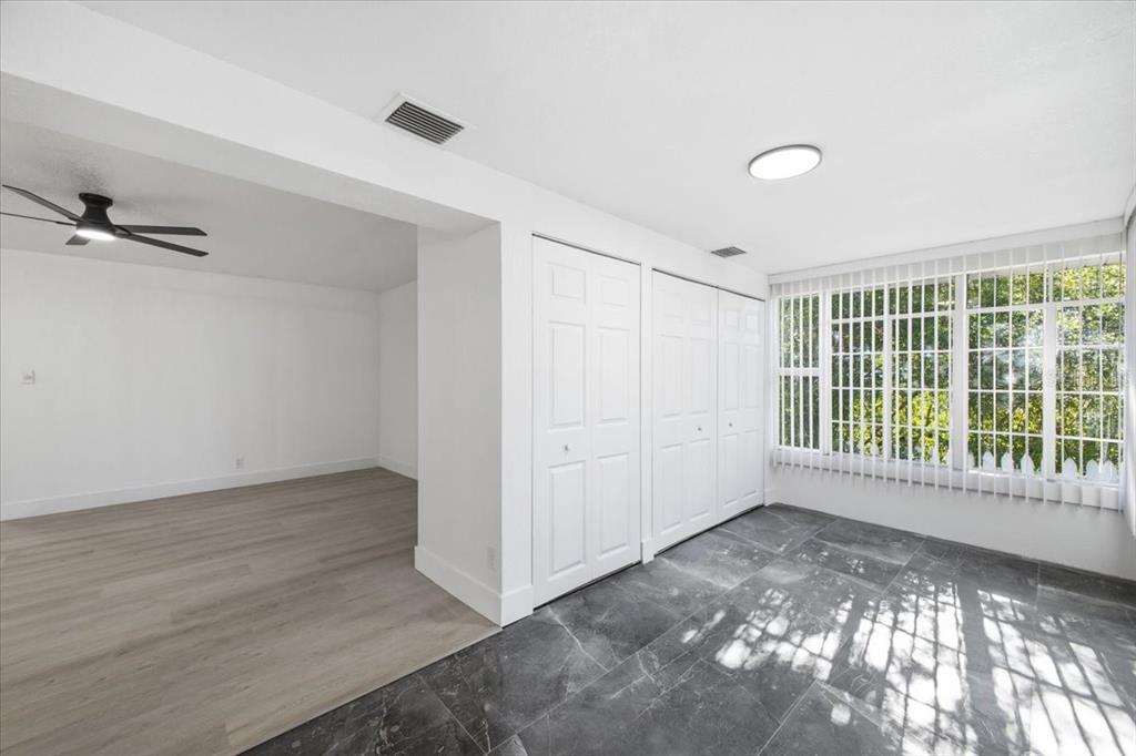 A room with dark tile flooring, white closets, and large windows, adjacent to a wood-floored area — 3308 3RD AVENUE W, BRADENTON, FL