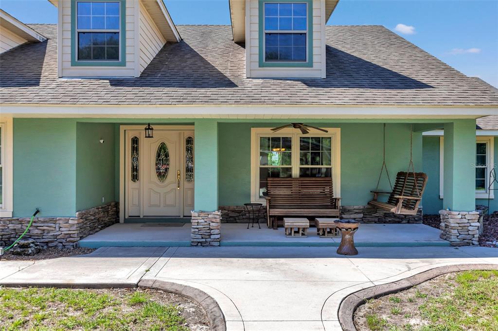 The exterior of a light green house features a covered porch with stone-based columns — 3325 S HWY 314A, OCKLAWAHA, FL