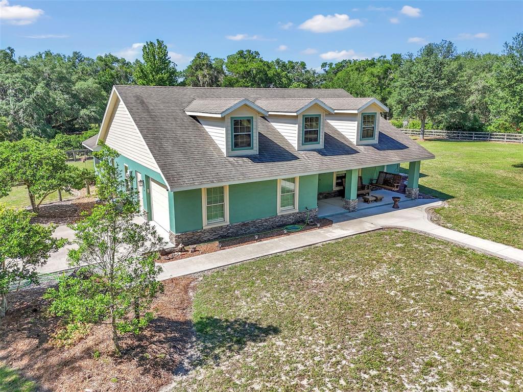 An aerial view of a green house with a porch, stone base, and three dormers — 3325 S HWY 314A, OCKLAWAHA, FL