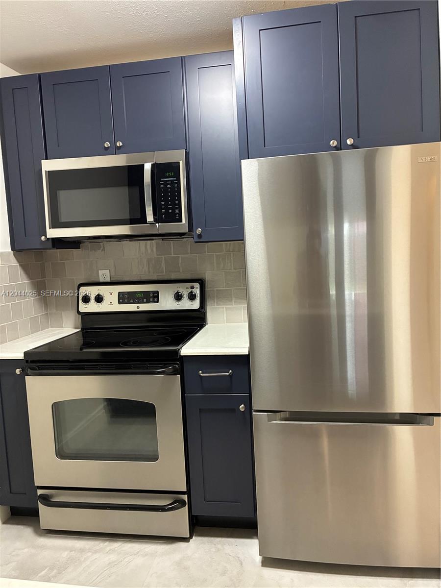 A kitchen features dark blue cabinets, stainless steel appliances, and a light-colored subway tile backsplash — 153 NE 141st St # B, Miami FL 33161, MIAMI, FL