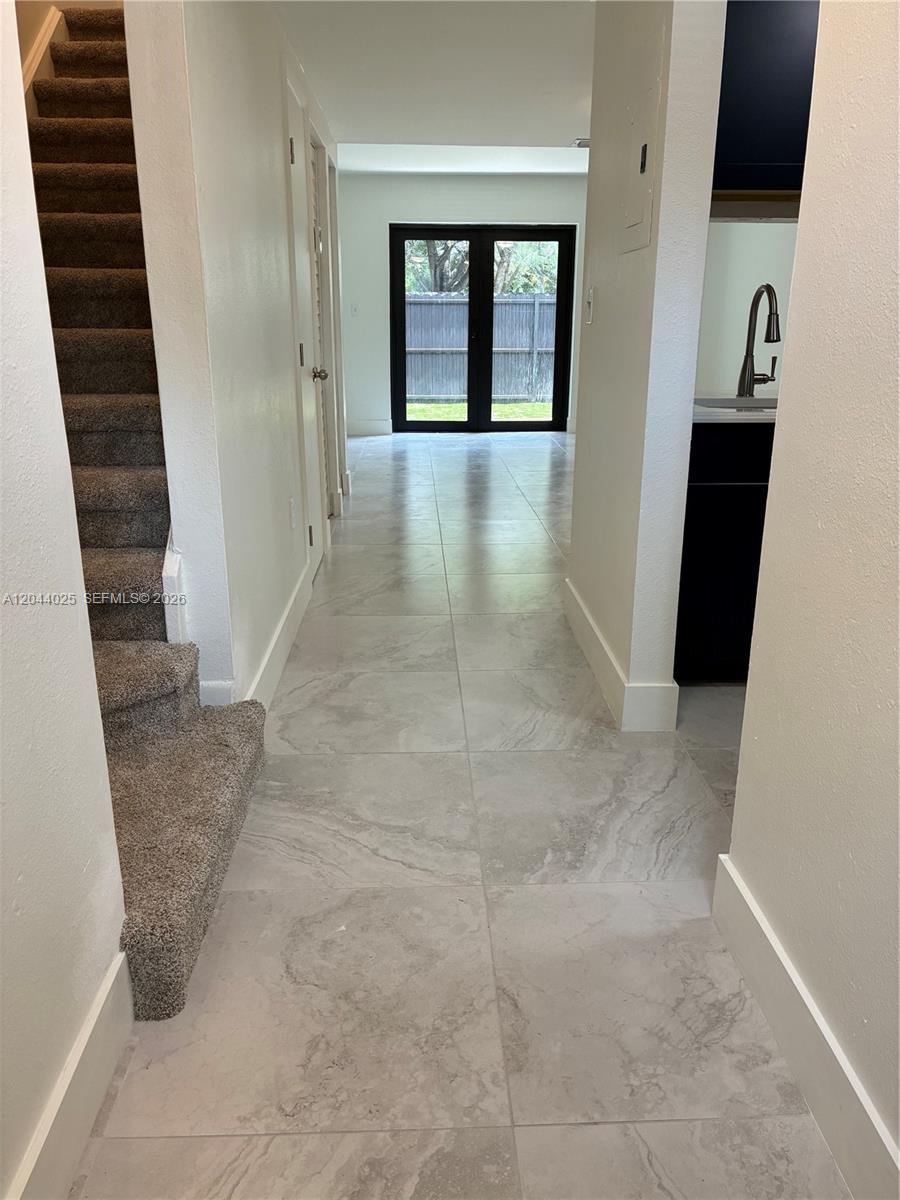 A hallway with carpeted stairs leads to a tiled living area with glass doors — 153 NE 141st St # B, Miami FL 33161, MIAMI, FL
