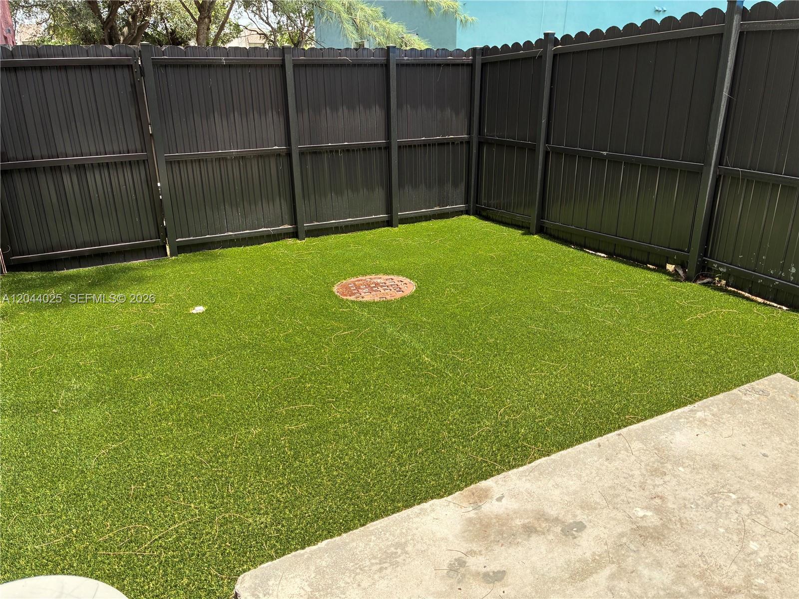 A fenced backyard features artificial turf and a circular utility access cover — 153 NE 141st St # B, Miami FL 33161, MIAMI, FL
