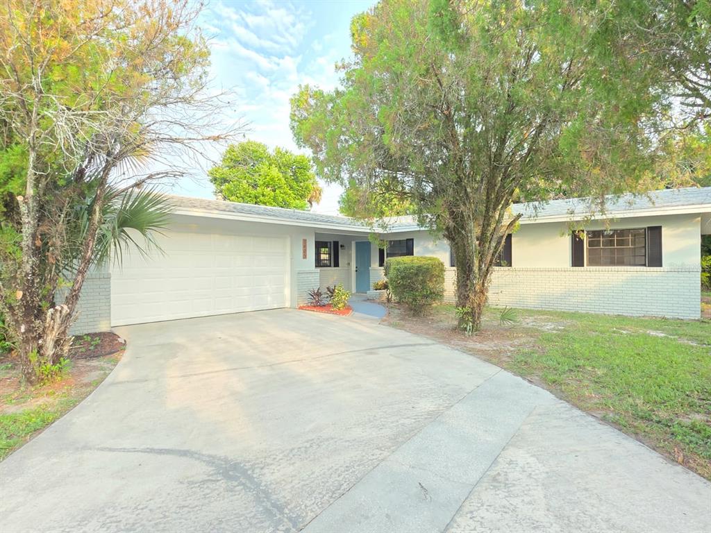 A single-story house with a white garage, light-colored brick exterior, and a concrete driveway — 1405 COUNTRY CLUB BOULEVARD, TITUSVILLE, FL