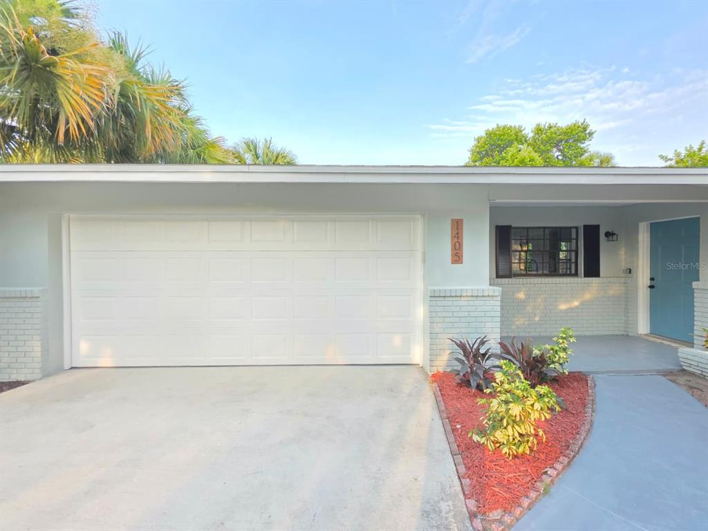 A light blue house exterior features a white garage door, a front door, and landscaping — 1405 COUNTRY CLUB BOULEVARD, TITUSVILLE, FL