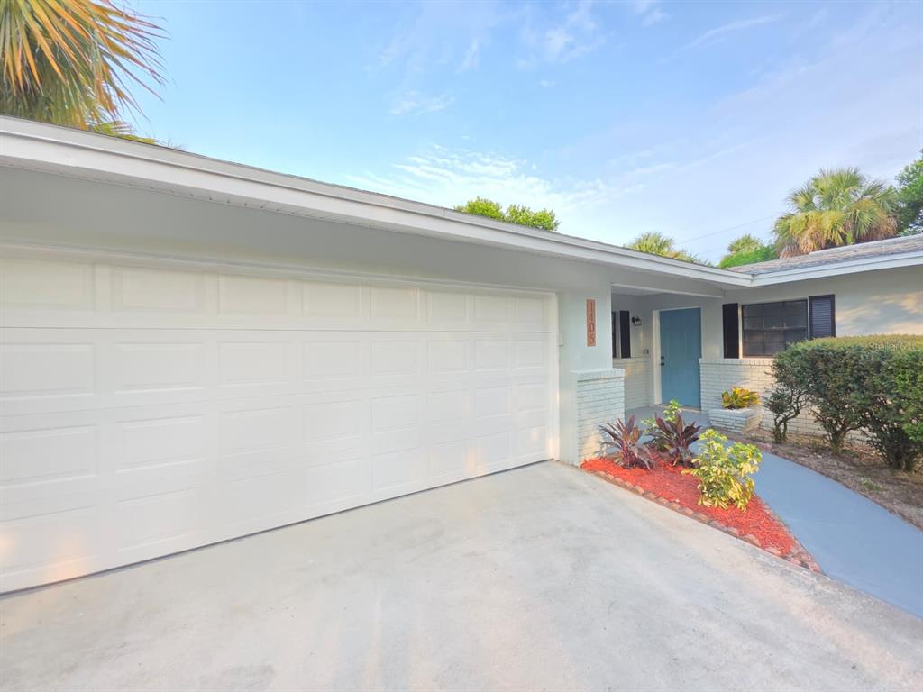 A white garage door, a blue front door, and a landscaped garden bed — 1405 COUNTRY CLUB BOULEVARD, TITUSVILLE, FL