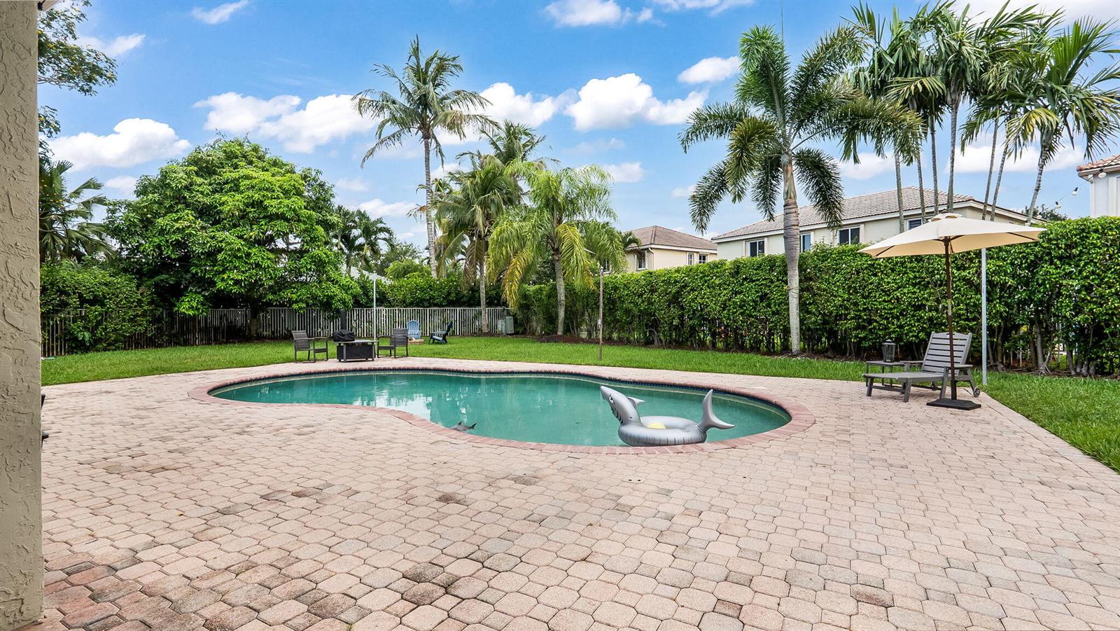 A backyard features a kidney-shaped swimming pool, a paved patio, and palm trees — 4411 Stone Ridge Way, Weston FL 33331, WESTON, FL