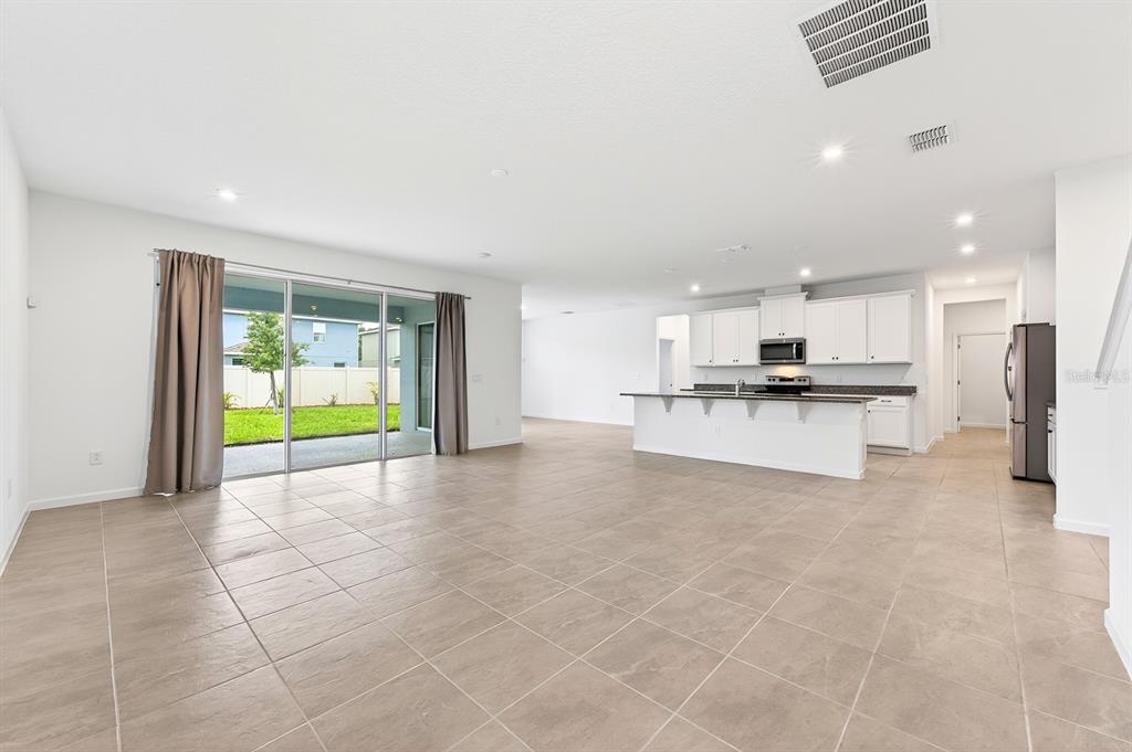 An open-concept kitchen and living area features light tile flooring and sliding glass patio doors — 891 HONEY PETAL LANE, DELAND, FL