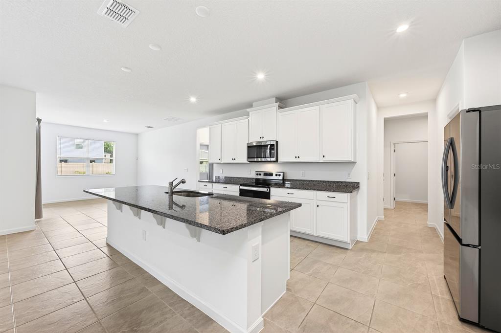 A kitchen featuring white cabinets, granite countertops, a large island, and stainless steel appliances — 891 HONEY PETAL LANE, DELAND, FL