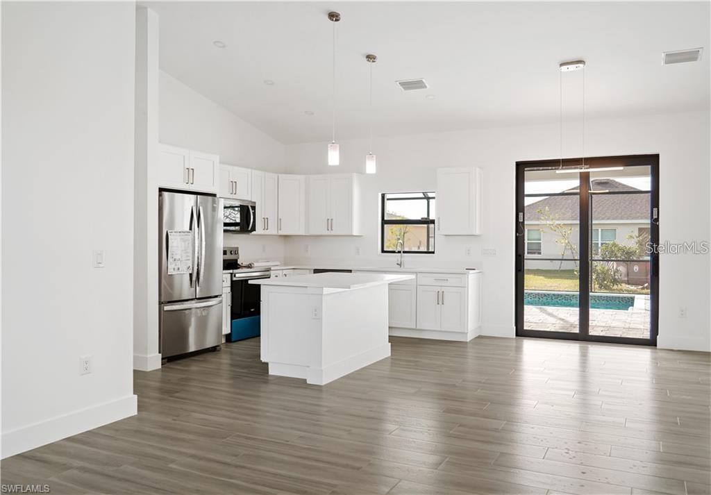 A modern kitchen features white cabinetry, stainless steel appliances, a center island, and wood-look flooring — 1436 NW 31ST AVENUE, CAPE CORAL, FL