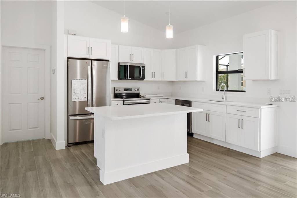 A modern kitchen features white cabinets, stainless steel appliances, a central island, and wood-look flooring — 1436 NW 31ST AVENUE, CAPE CORAL, FL