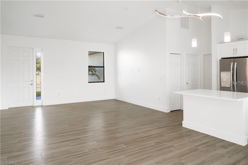 A bright, open-concept living area features white walls, wood-look tile flooring, and a kitchen island — 1436 NW 31ST AVENUE, CAPE CORAL, FL