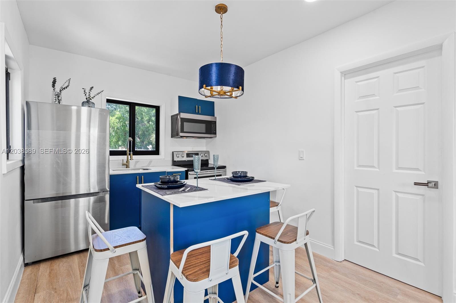 A kitchen features blue cabinets, a white island with seating, and stainless steel appliances — 1824 NW 47th St # A, Miami FL 33142, MIAMI, FL