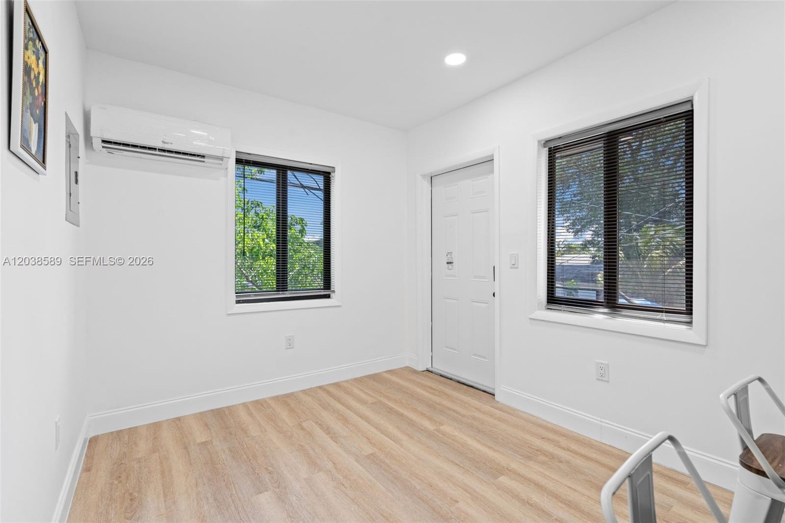 A bright, empty room features white walls, light wood-look flooring, two windows, and a mini-split — 1824 NW 47th St # A, Miami FL 33142, MIAMI, FL