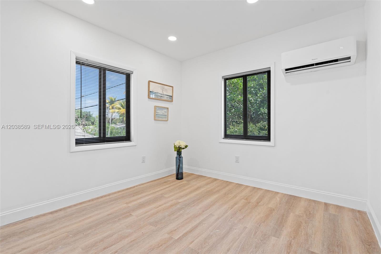 A bright, empty room features light wood-look flooring, white walls, two windows, and a wall-mounted AC — 1824 NW 47th St # A, Miami FL 33142, MIAMI, FL