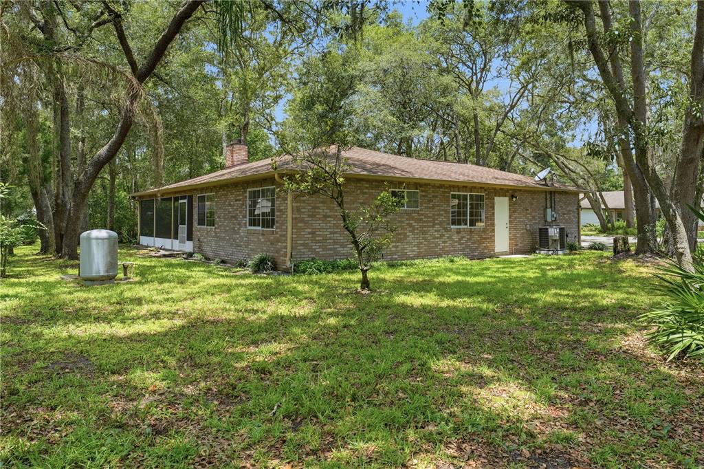 A brick house with a screened porch and a propane tank in a wooded yard — 1356 6TH STREET, ORANGE CITY, FL