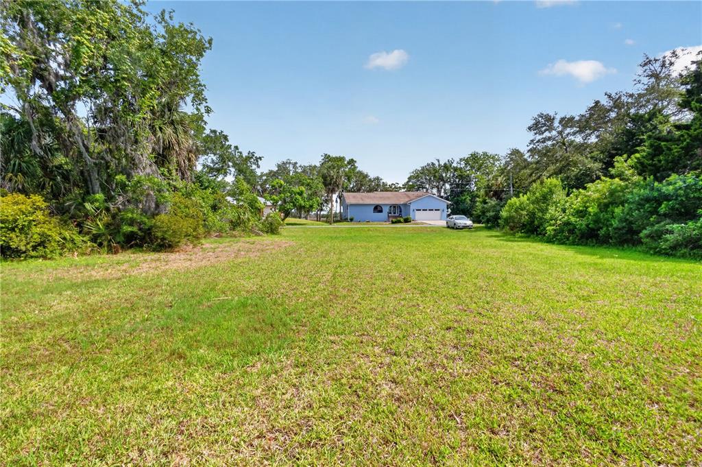 A large, grassy vacant lot sits in front of a blue single-story house — 4546 S SAWGRASS CIRCLE, HOMOSASSA, FL