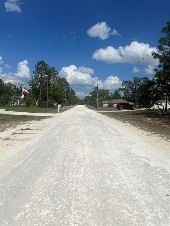 A gravel road stretches through a residential area with trees, houses, and a parked vehicle — SAGE THRASHER AVE, WEEKI WACHEE, FL