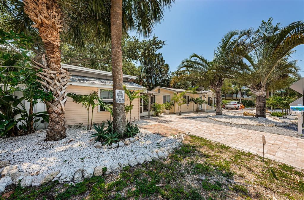 A light-colored cottage exterior features a brick walkway, palm trees, and white gravel landscaping — 201.5 7TH AVENUE, INDIAN ROCKS BEACH, FL