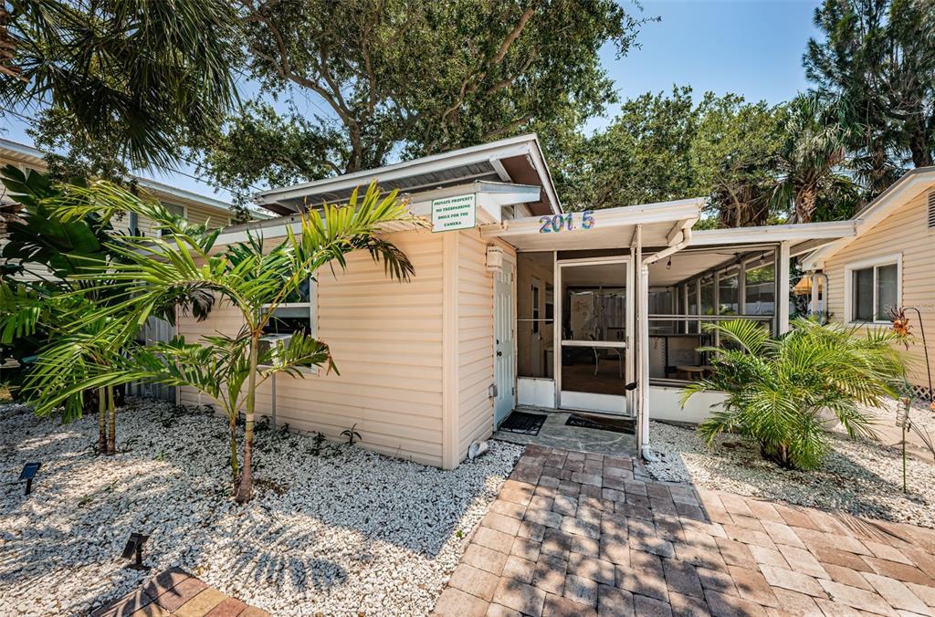 A light-colored cottage with a screened-in porch, a stone walkway, and palm trees — 201.5 7TH AVENUE, INDIAN ROCKS BEACH, FL