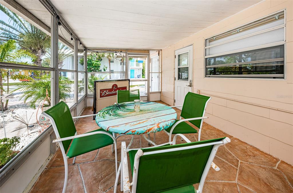 A screened-in porch features a round table with four green chairs and tiled flooring — 201.5 7TH AVENUE, INDIAN ROCKS BEACH, FL