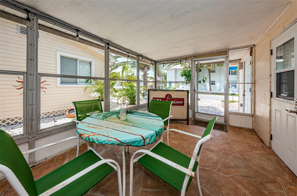 A screened-in porch features a round table with green chairs and a stone-patterned floor — 201.5 7TH AVENUE, INDIAN ROCKS BEACH, FL