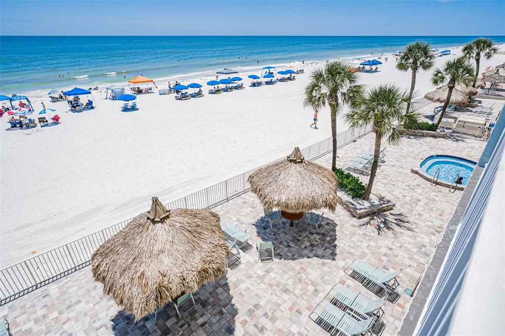 An elevated view of a beachside patio with tiki umbrellas, lounge chairs, and a hot tub — 17200 GULF BOULEVARD UNIT 202, NORTH REDINGTON BEACH, FL