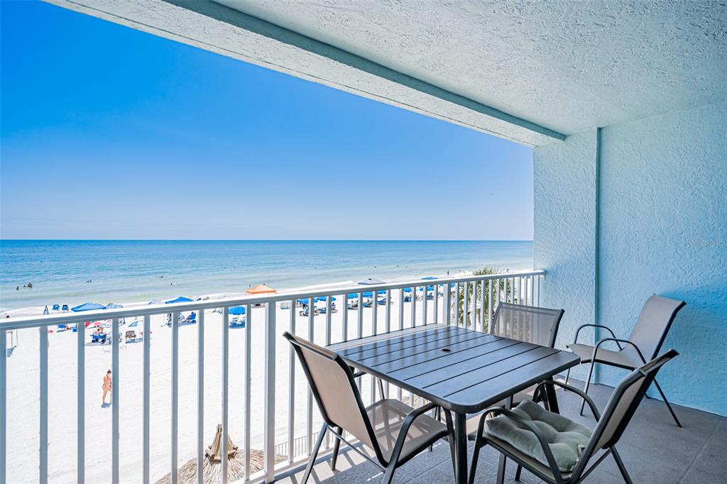 A balcony with a table and chairs overlooks a sandy beach and the ocean — 17200 GULF BOULEVARD UNIT 202, NORTH REDINGTON BEACH, FL