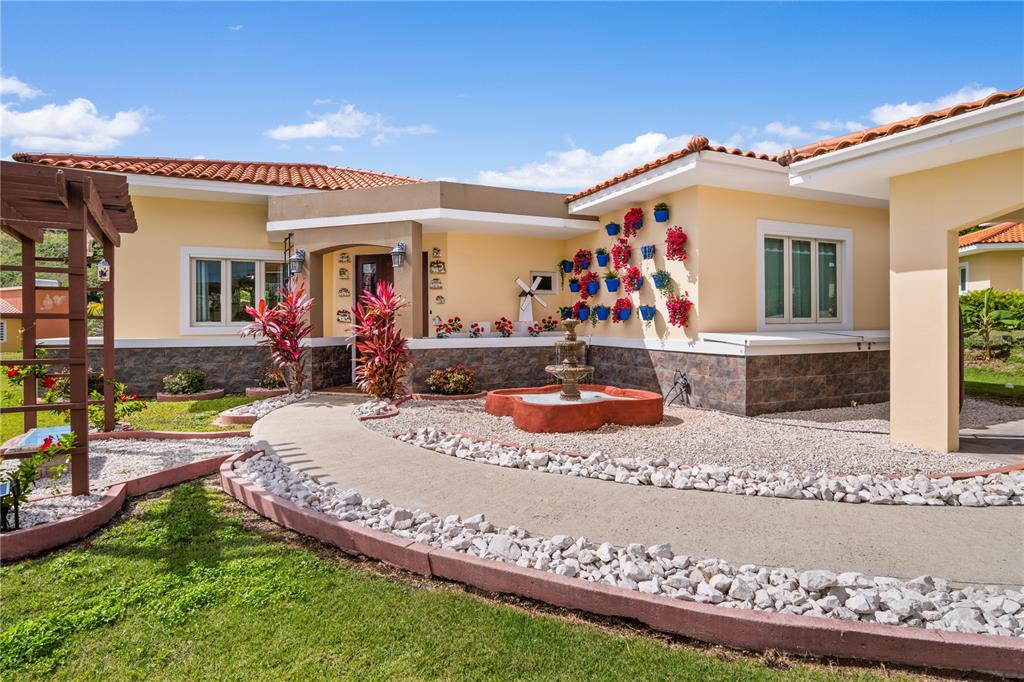 A yellow house features a stone-trimmed exterior, a curved walkway, and a small water fountain — Palmas del Mar THE VIEWS # 12, HUMACAO, PR