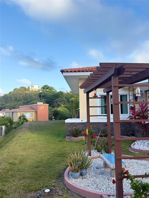 A wooden pergola stands over a gravel patio with a bench beside a residential house — Palmas del Mar THE VIEWS # 12, HUMACAO, PR