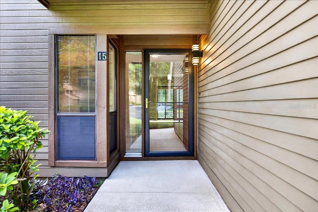 The exterior entrance of a home features tan horizontal siding, a glass storm door, and a window — 15 SHERBURY COURT, PALM COAST, FL