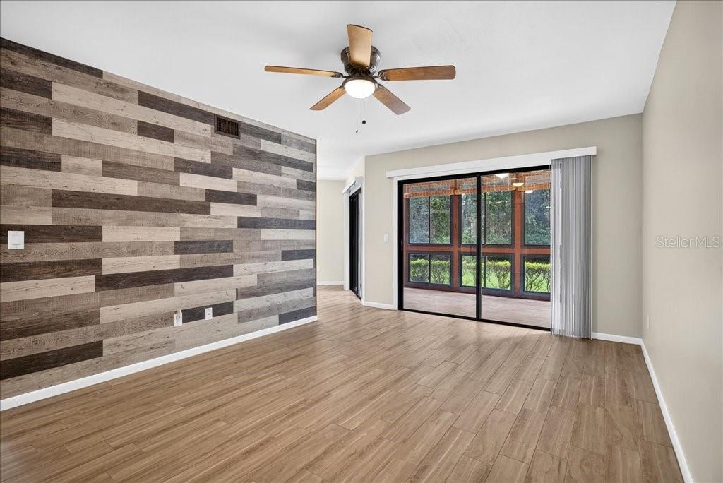 A living room features wood-look tile flooring, a ceiling fan, and a wood-plank accent wall — 15 SHERBURY COURT, PALM COAST, FL