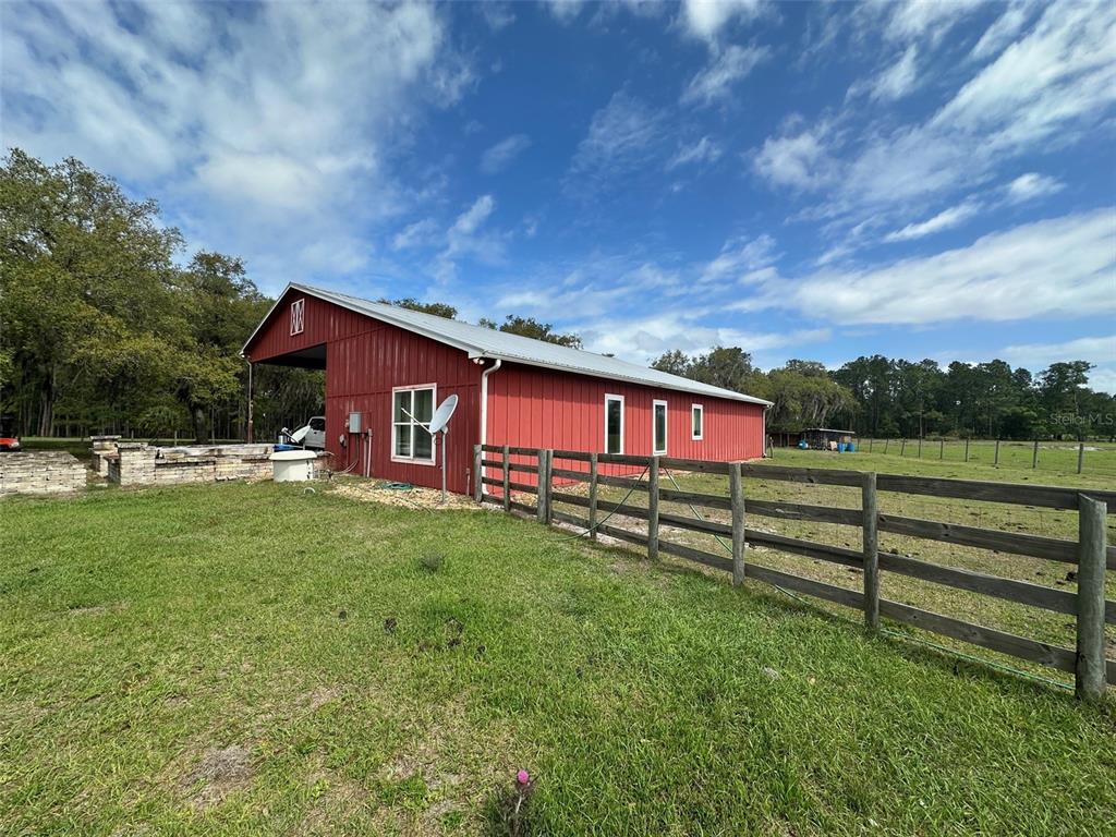 A red metal barn with a covered porch stands in a grassy field with fencing — 15120 SE 85TH STREET, OCKLAWAHA, FL