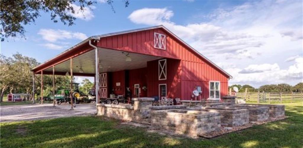 A red barn with a large covered porch and stone raised garden beds in front — 15120 SE 85TH STREET, OCKLAWAHA, FL